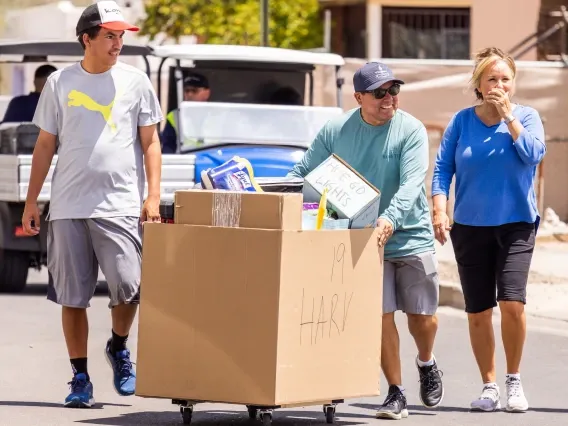 a family walking behind a large rolling bin with household items in it